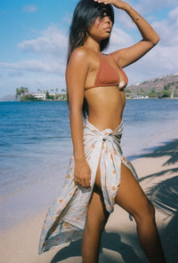 Woman in a bikini and sarong standing on a beach with ocean and sky in the background