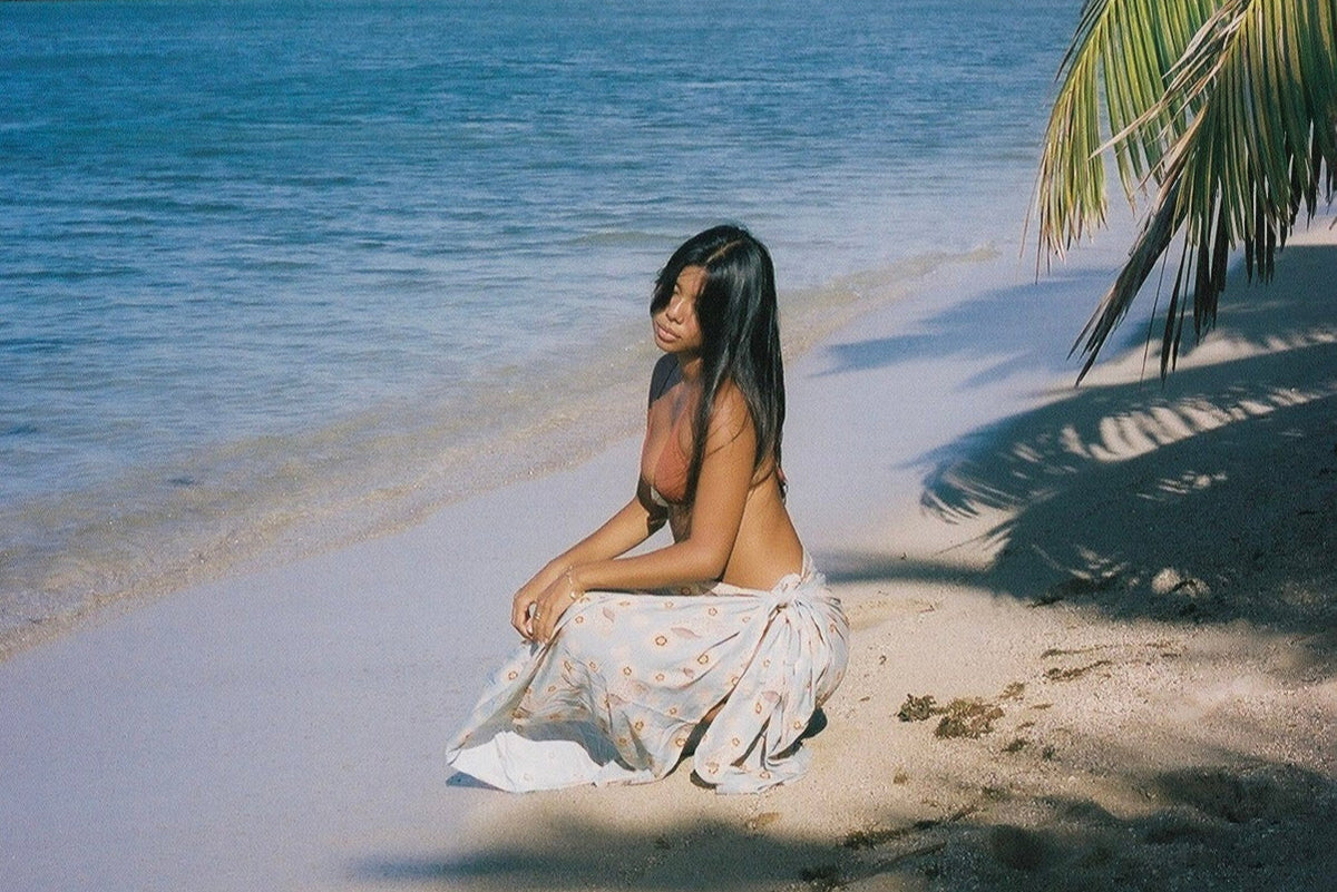 Woman sitting on a sandy beach with ocean and palm tree in the background