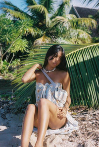 Woman in a white dress sitting under a palm tree on a beach