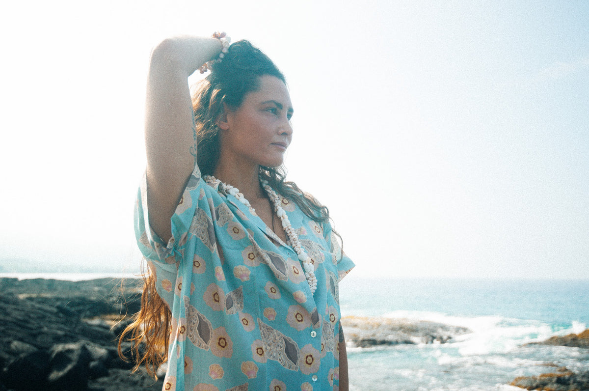 A person standing on a beach wearing a short-sleeved shirt dress with a floral pattern on a baby blue background.