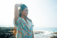 A person standing on a beach wearing a short-sleeved shirt dress with a floral pattern on a baby blue background.