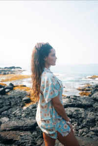 A person standing on a beach wearing a short-sleeved shirt dress with a floral pattern on a baby blue background.