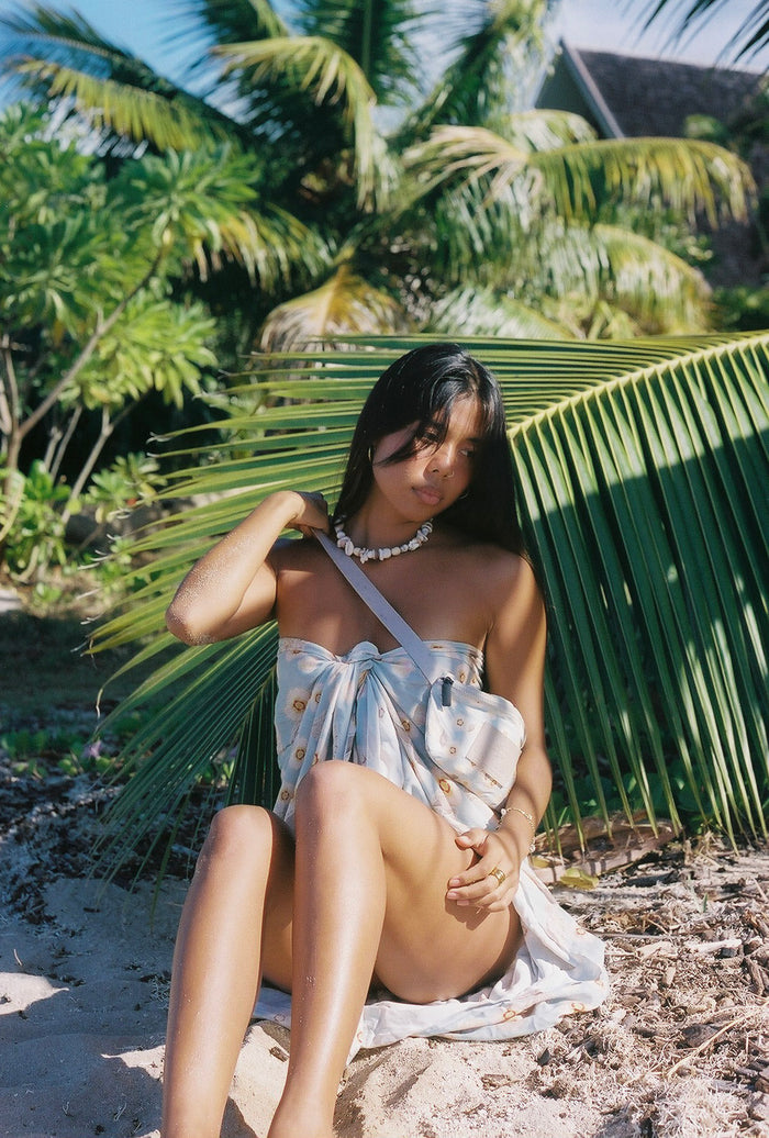 Woman in a white dress sitting under a palm tree on a beach