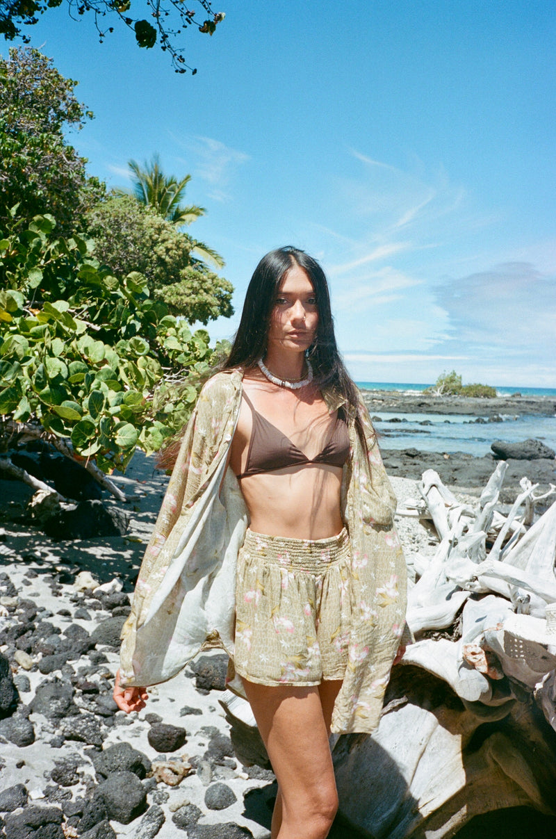 Woman standing on a rocky beach with greenery and ocean in the background