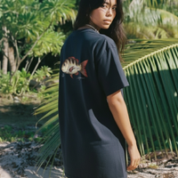 Woman wearing a black t-shirt with a fish design on the back, standing in a tropical setting with palm trees.