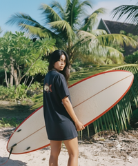 Person holding a surfboard on a beach with palm trees in the background