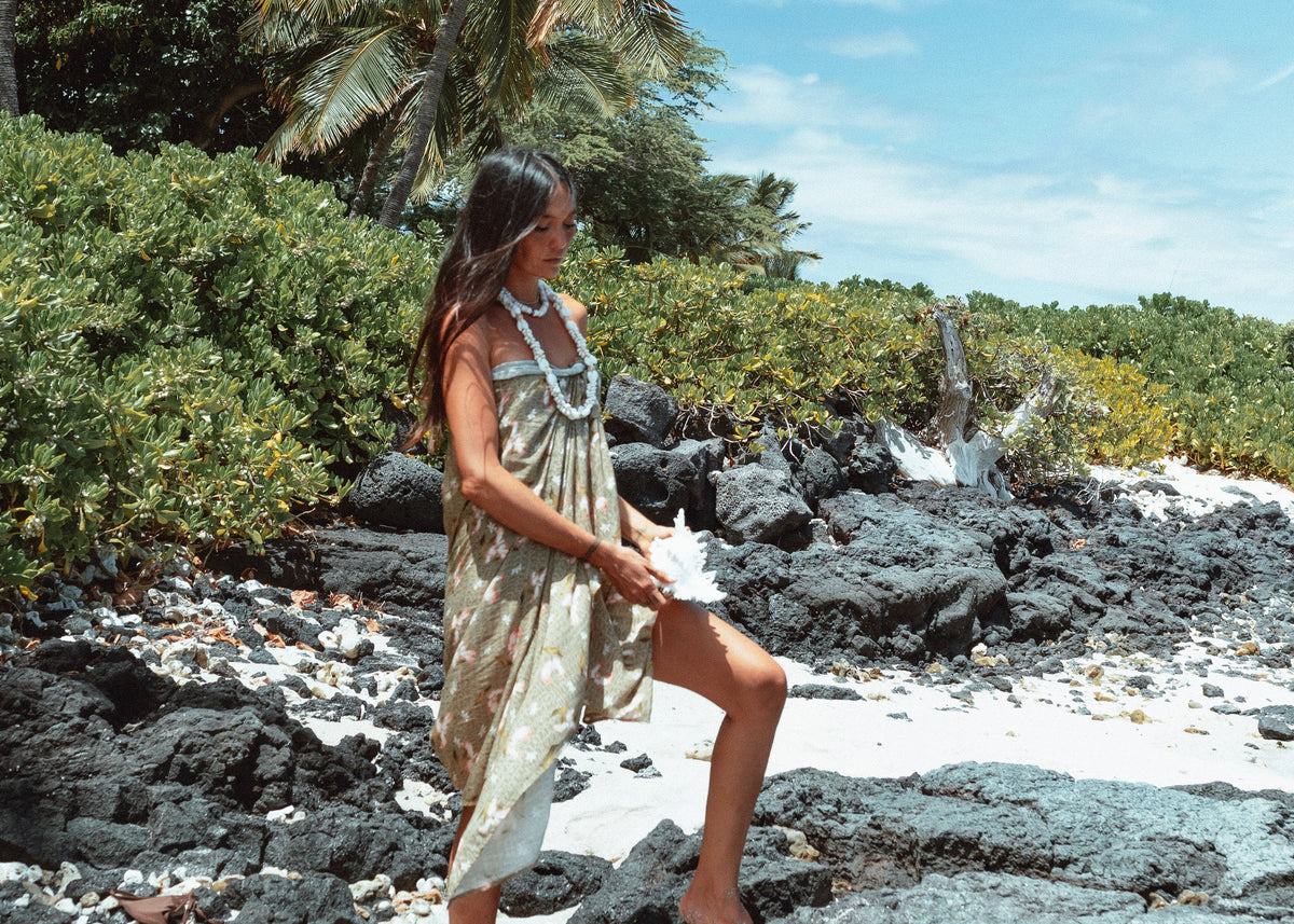 Woman in a dress standing on a rocky beach with palm trees in the background