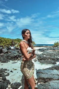 Woman in a green dress standing on a rocky beach with ocean and sky in the background