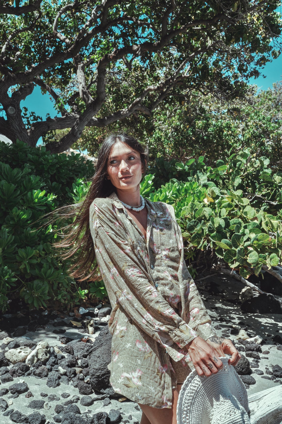 Woman in a light dress standing in a natural setting with greenery and rocks.
