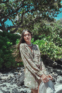 Woman in a light dress standing in a natural setting with greenery and rocks.